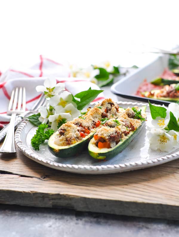 Two zucchini boats served on a white plate. Each zucchini half is filled with a beef and vegetable mixture and topped with a Parmesan breadcrumb mixture.