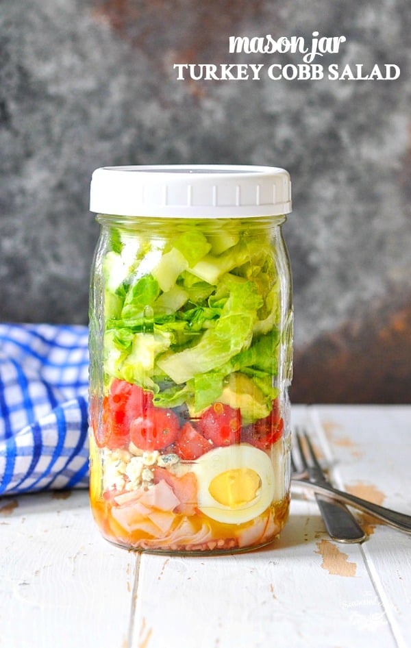 A mason jar filled with turkey cobb salad with a white lid