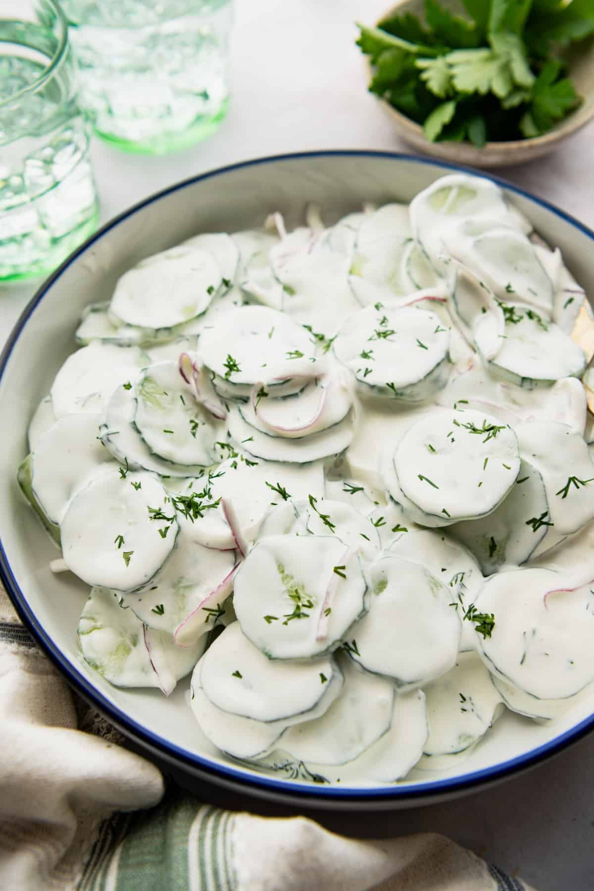 Close up side shot of a creamy cucumber salad in a blue and white bowl.