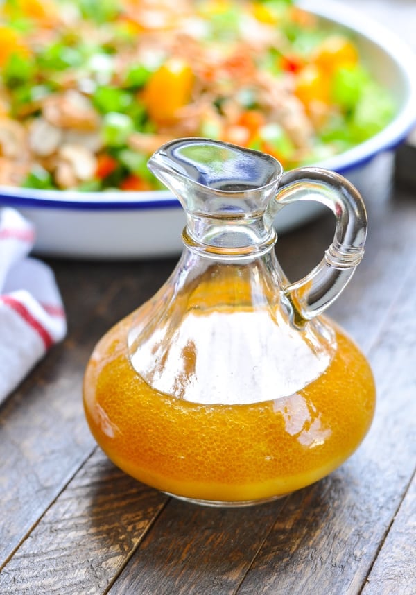 A small glass bottle partially filled with an orange-colored salad dressing.