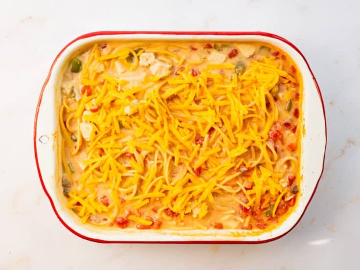 Adding cheese to the top of a chicken spaghetti bake.