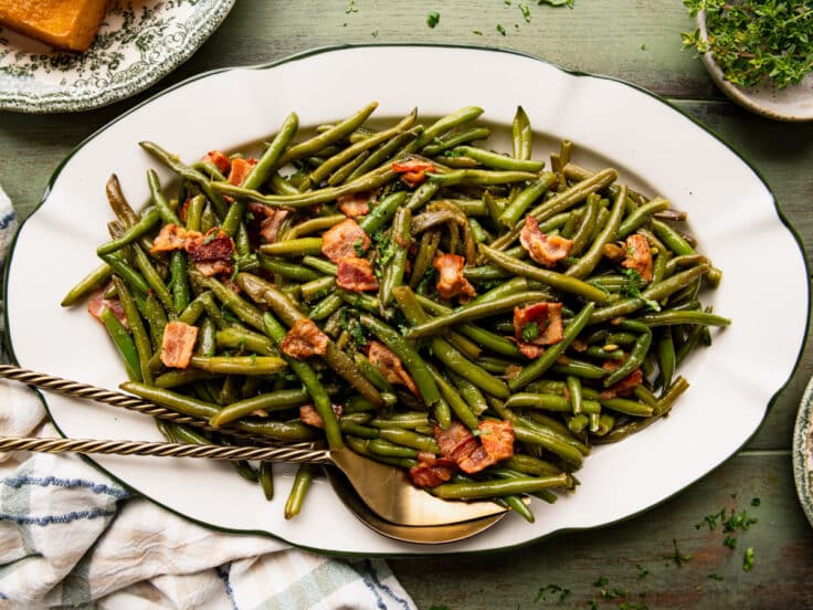Horizontal overhead image of slow cooker green beans with bacon on a white serving platter.
