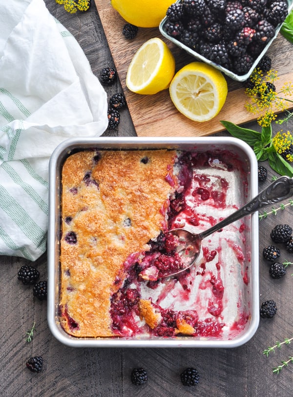 The best blackberry cobbler in a baking dish with blackberries scattered around at the side