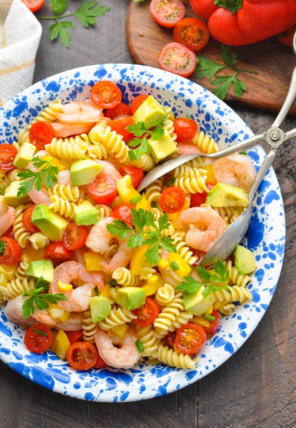 An overhead shot of a shrimp pasta salad with tomatoes and avocado on a blue and white spotted plate