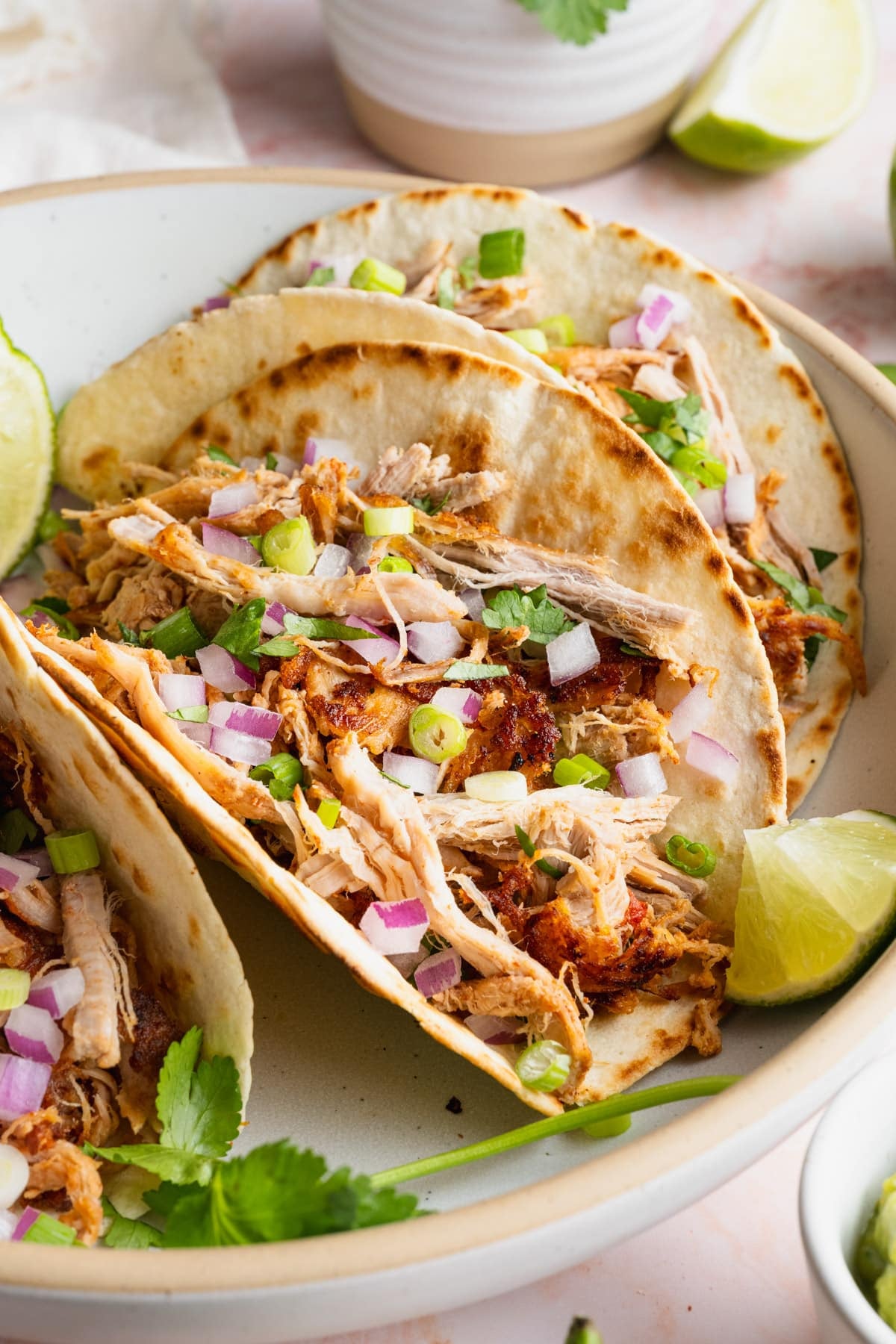 Side shot of slow cooker carnitas used to make Mexican pulled pork tacos in a white bowl.