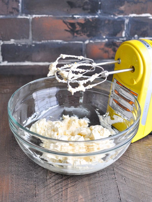 Glass bowl with crab dip ingredients and an electric mixer