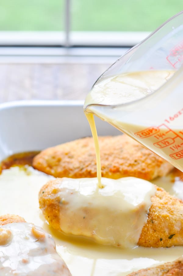 Pouring creamy gravy over golden baked chicken breasts