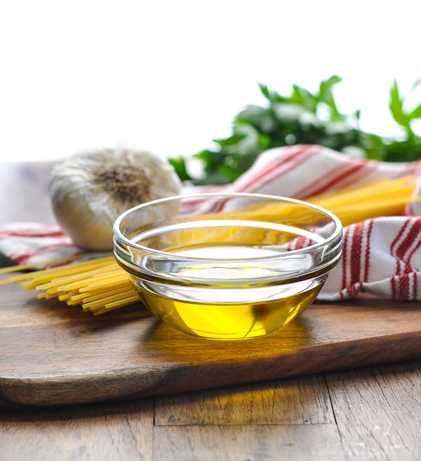 The ingredients needed to make spaghetti aglio e olio - spaghetti, oil, and garlic, set out on a wooden cutting board.