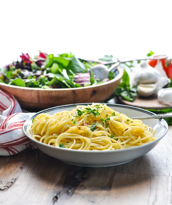 A bowl full of spaghetti aglio e olio served with a fresh mixed greens salad in the background.
