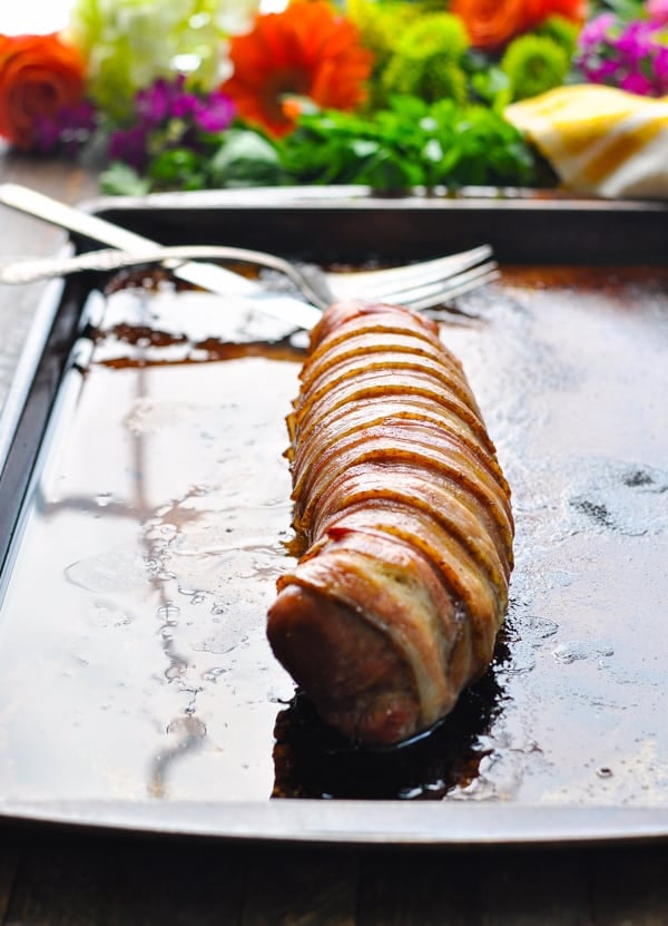 Bacon wrapped pork tenderloin unsliced on a baking sheet