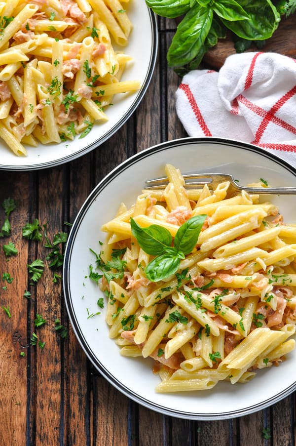 Bowl of penne with prosciutto cream sauce garnished with fresh basil and parsley