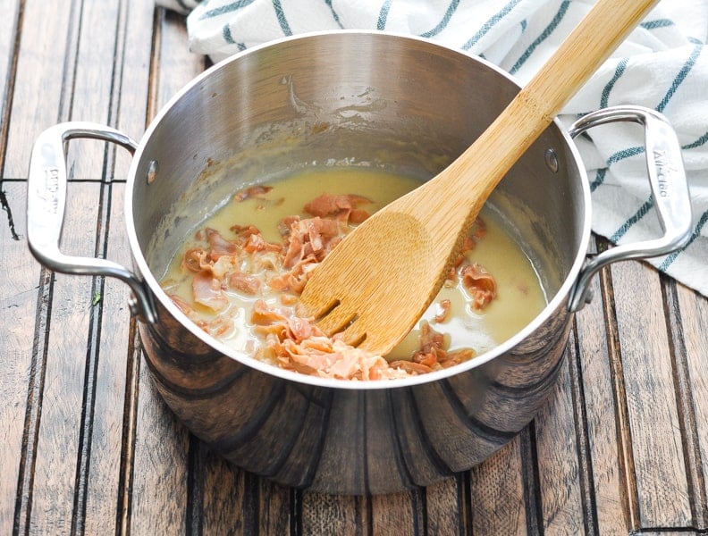 Prosciutto Parmesan Cream Sauce for pasta in a saucepan with wooden spoon