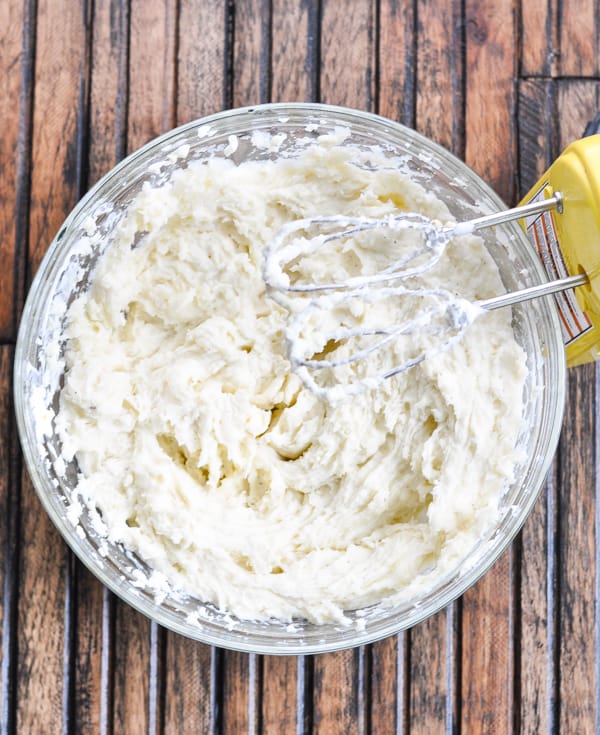 Whipped mashed potatoes in glass bowl with hand mixer