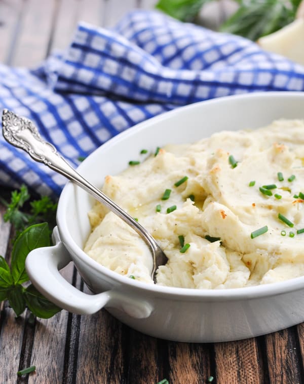 Make ahead garlic mashed potatoes in white baking dish with silver spoon