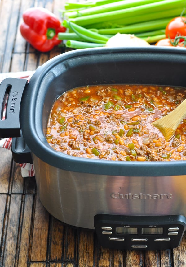 Cowboy pork and beans cook in a large silver Cuisinart slow cooker.