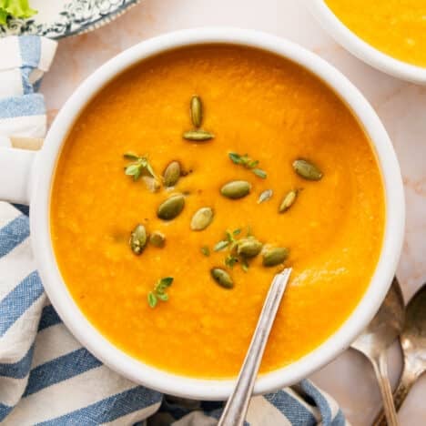Square overhead shot of two bowls of healthy and easy pumpkin soup served in white bowls with pumpkin seeds on top for a garnish.
