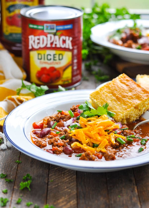 A hearty bowl full of chili con carne, garnished with shredded cheddar cheese and served with a side of cornbread.