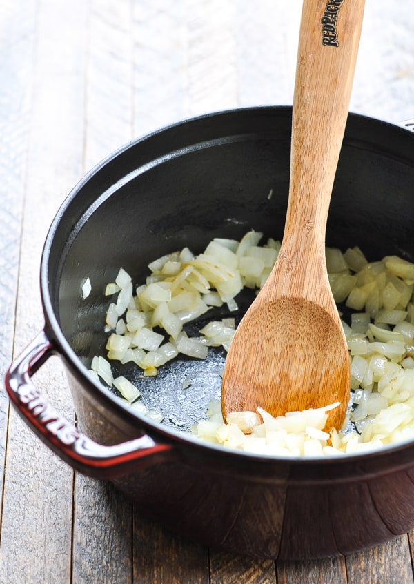 Chopped onions sauteed in a cast iron pot with a wooden spoon.