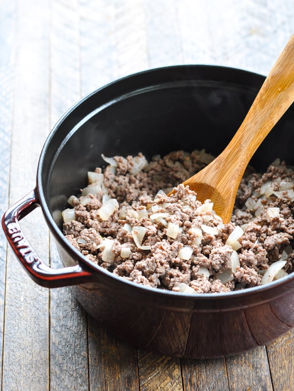 Cooked ground beef mixed with diced onions in a pot - the base of chili con carne.