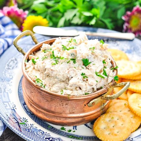 Square side shot of a bowl of crab dip with crackers on a plate