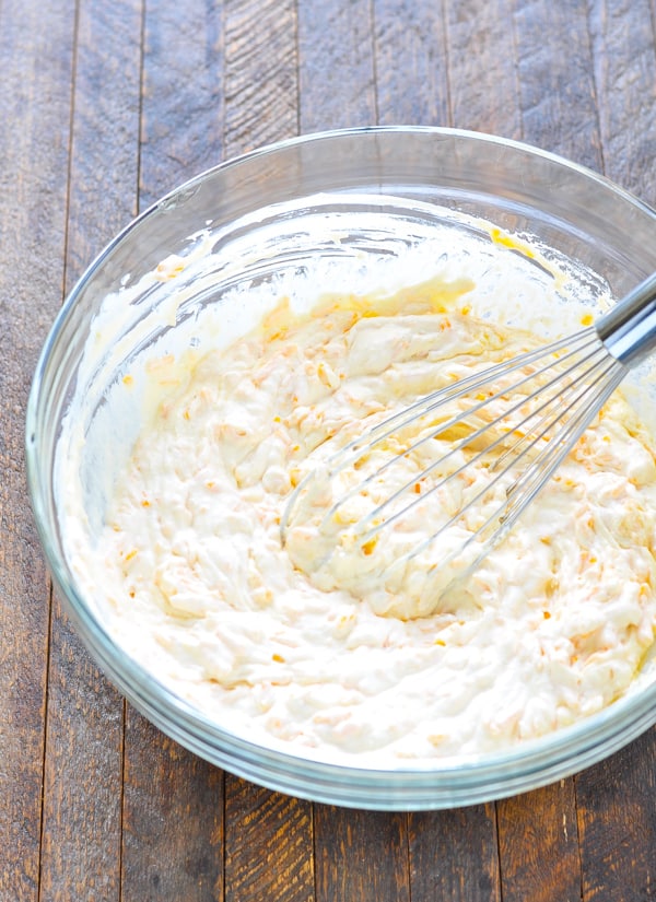 Sour cream mixture for hash brown casserole in glass mixing bowl with whisk