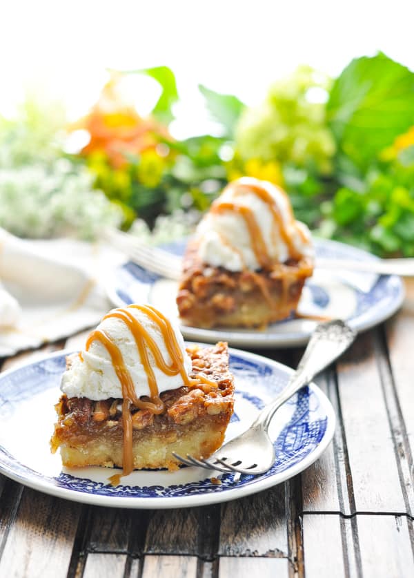 Pecan pie bars on blue and white plates with vanilla ice cream and caramel sauce