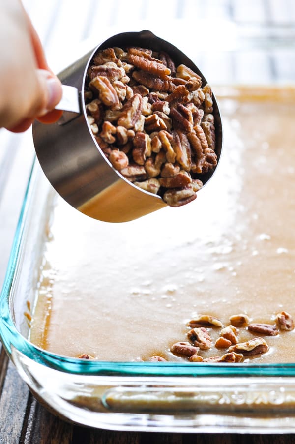 Sprinkling chopped pecans over pecan pie bars filling