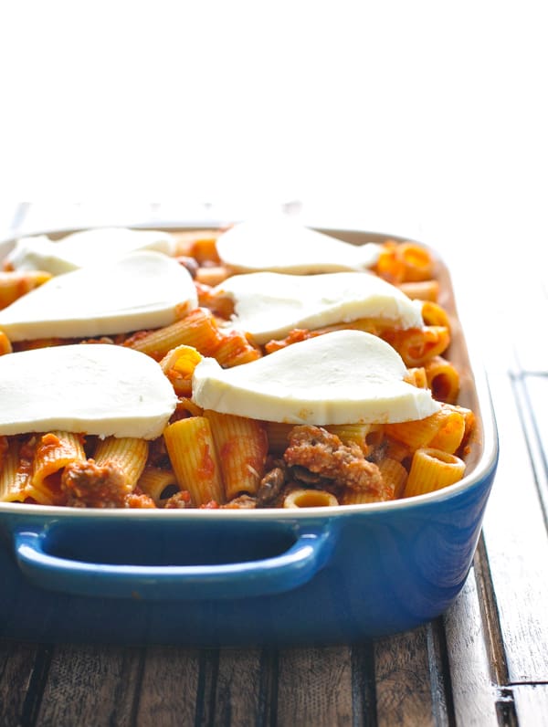 A side-angle shot of Italian sausage pasta bake topped with slices of fresh mozzarella cheese, ready to be baked in the oven.