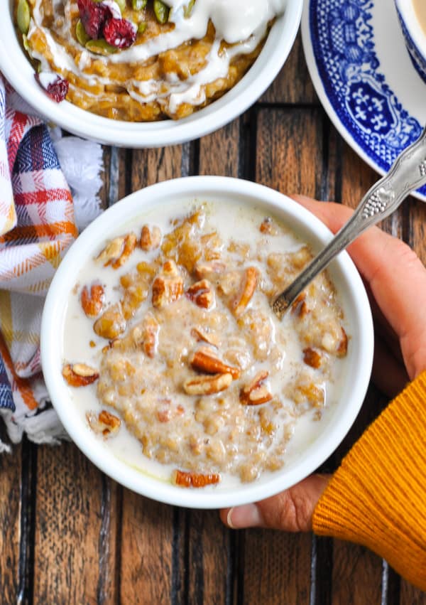 Holding bowl of healthy slow cooker oatmeal topped with pecans