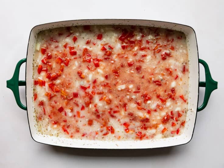 Adding rice and tomatoes to a creamy sauce in a baking dish.