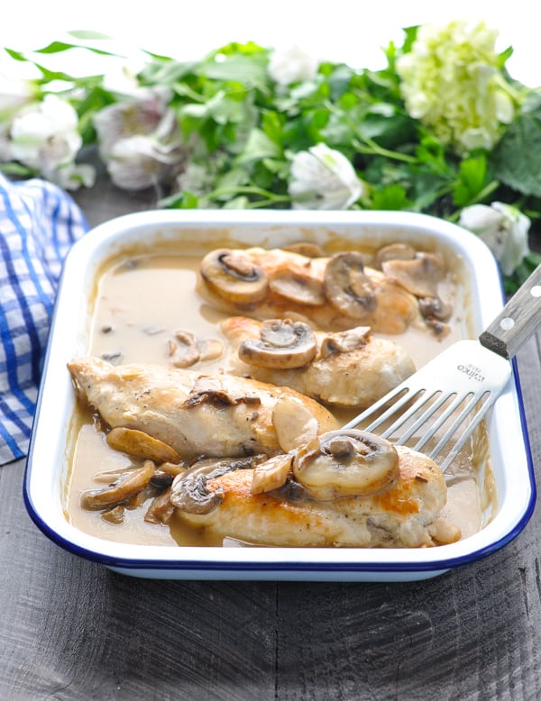 Baked chicken breasts with creamy mushroom sauce in white baking dish with spatula
