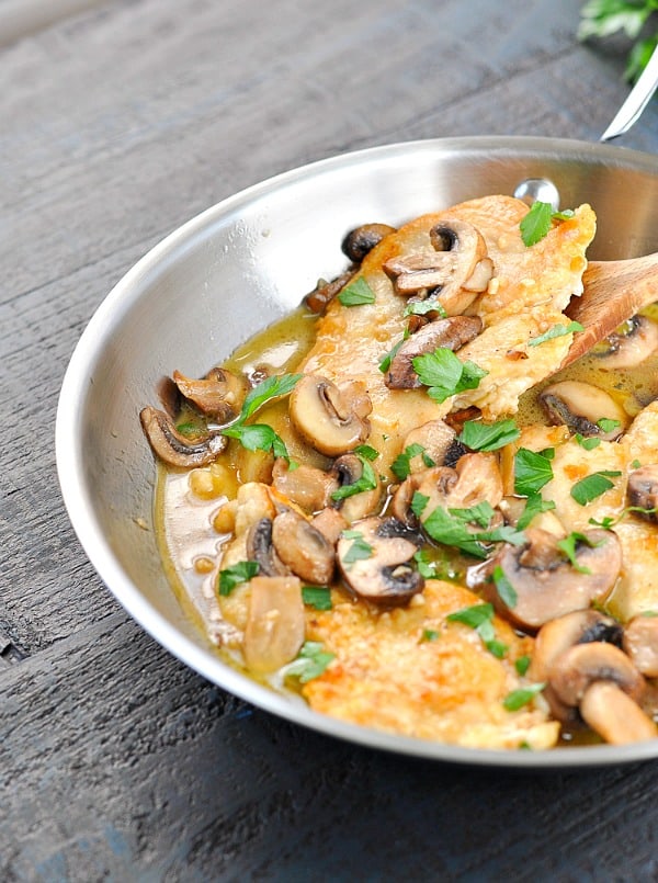 Slice of chicken marsala on a wooden spoon in a skillet with mushrooms