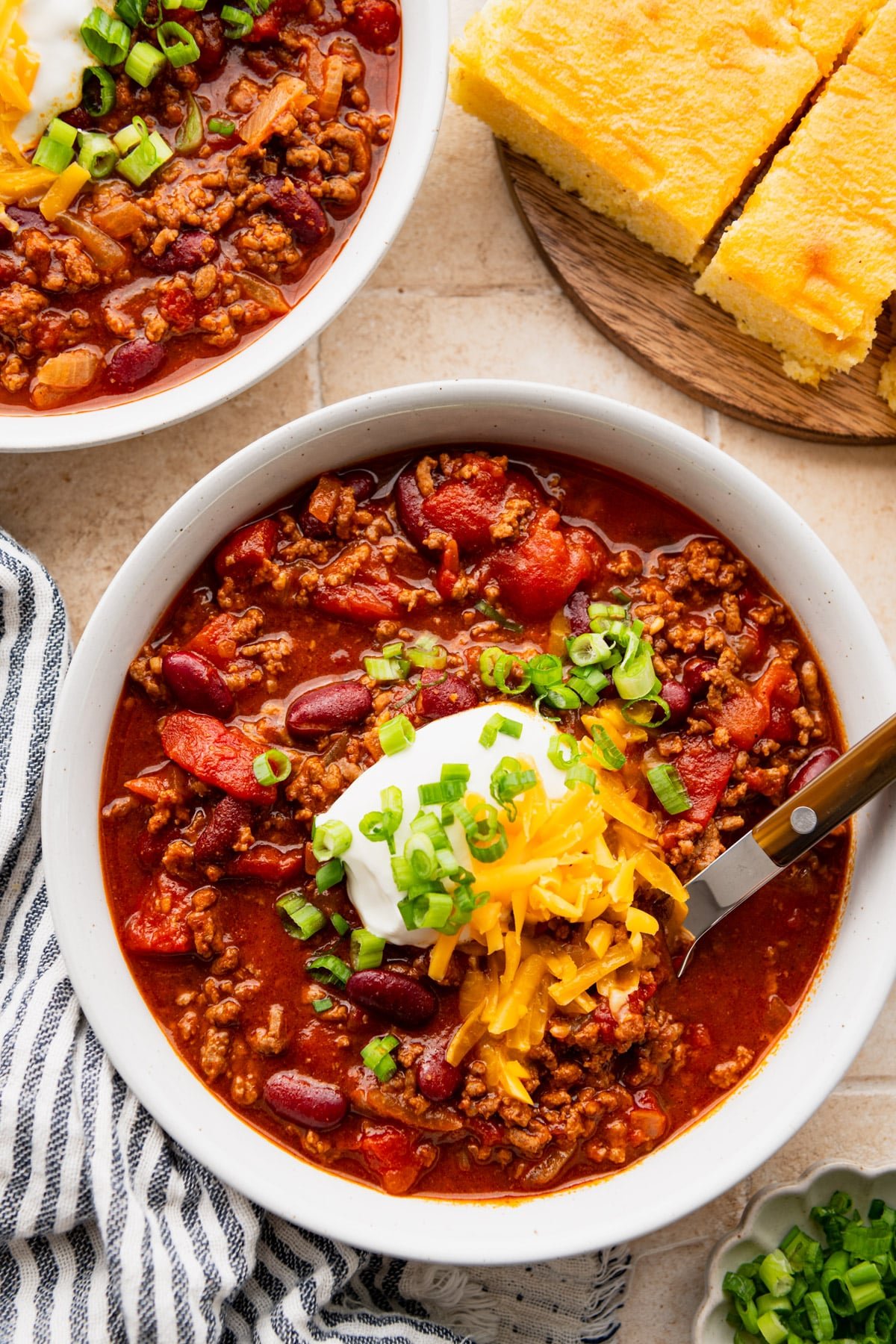 Overhead image of two bowls of chili con carne on a table with cornbread.
