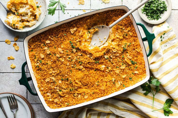 Horizontal overhead shot of a serving spoon in a dish of baked funeral potatoes.