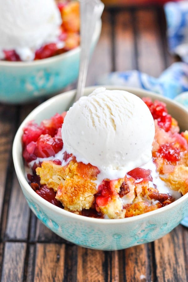 Turquoise bowl with warm cherry dump cake, spoon and vanilla ice cream on top
