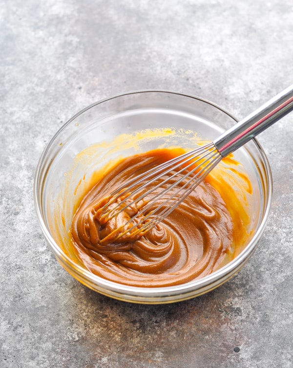Peanut sauce with a whisk in a glass mixing bowl