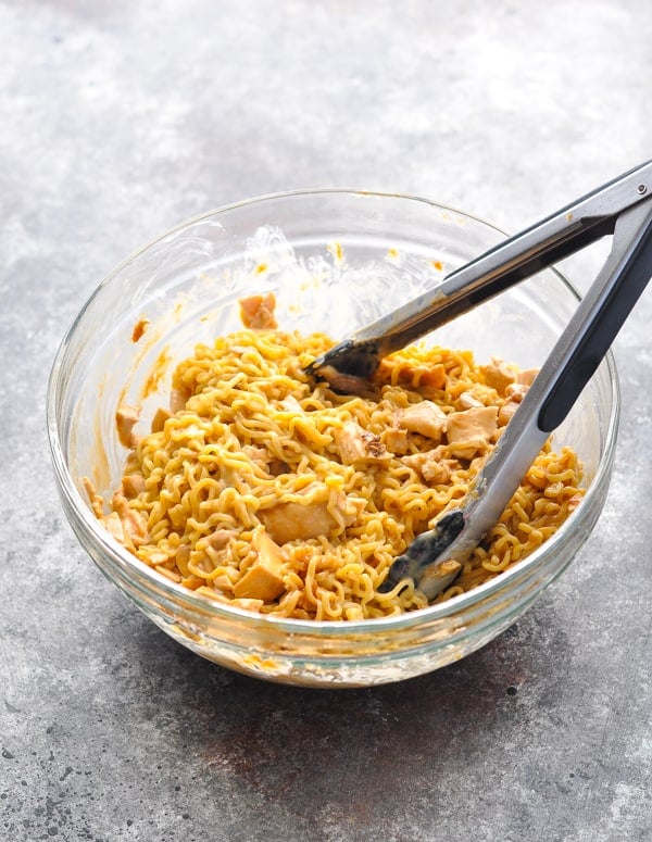 Cooked ramen noodles combined with peanut sauce and chicken in a glass bowl