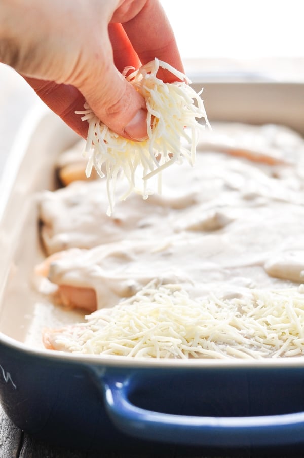 Sprinkling mozzarella cheese over chicken in casserole dish