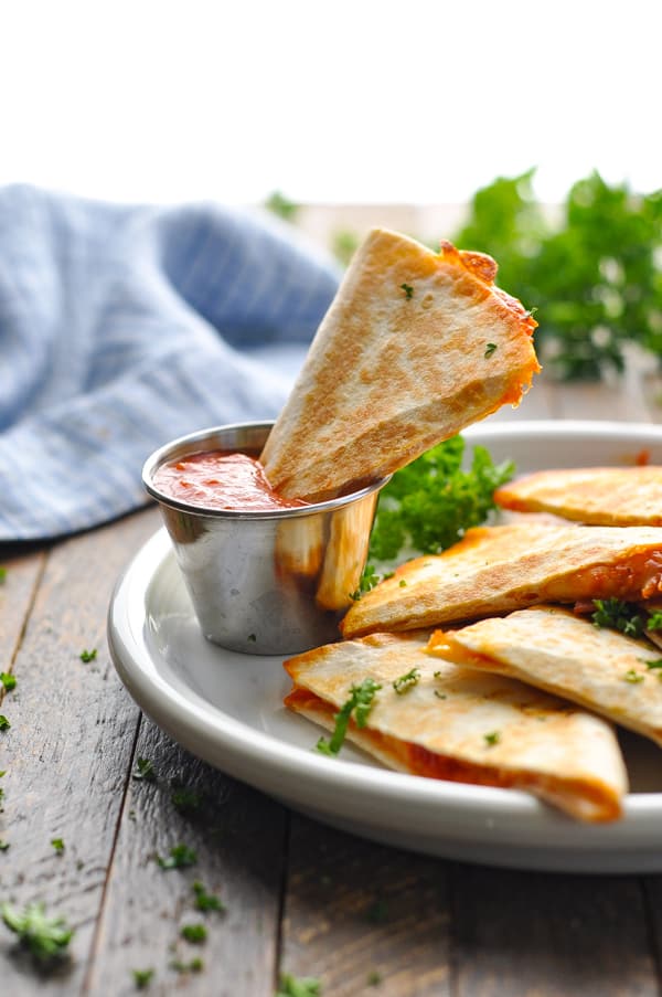 Pizza quesadilla triangle in a cup of marinara for dipping