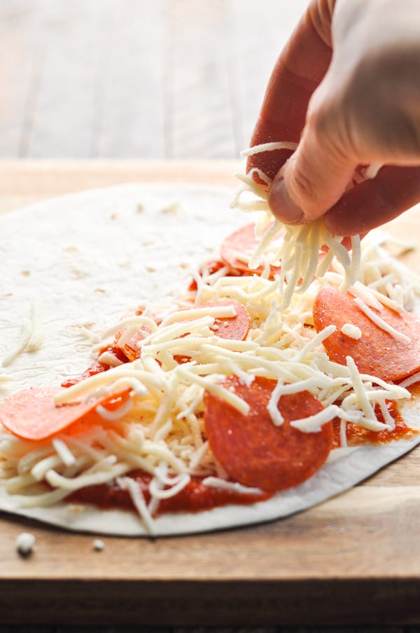 Sprinkling more mozzarella cheese on top of pizza quesadilla