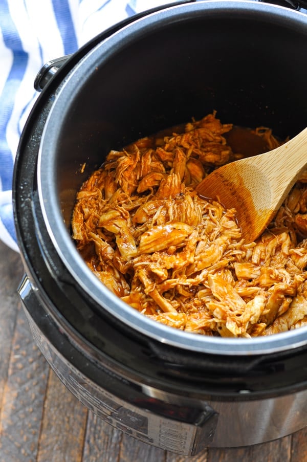Shredded barbecue chicken in the Instant Pot with wooden spoon
