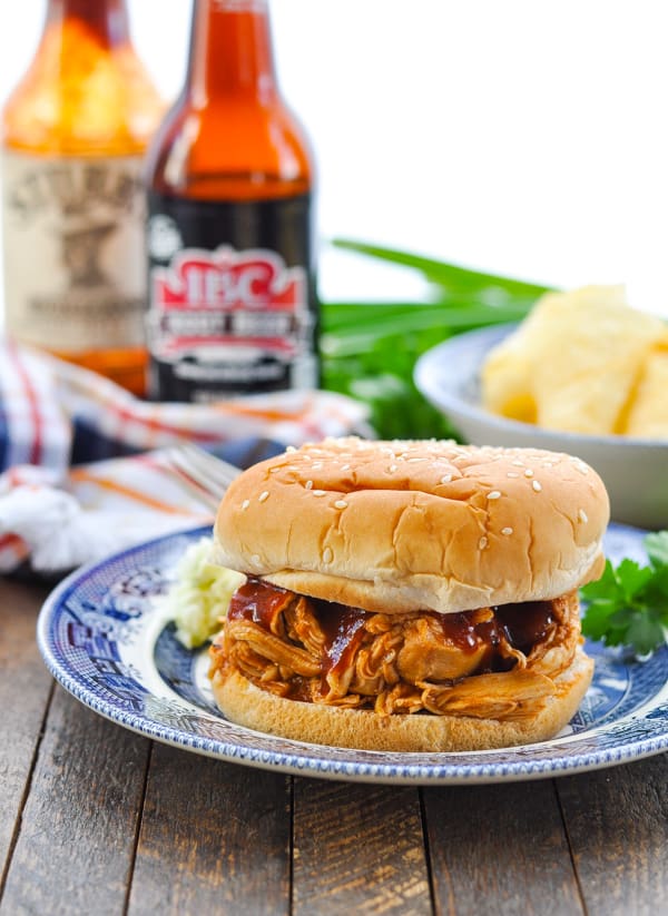 Barbecue chicken sandwich on a blue willow plate with root beer bottle in the background
