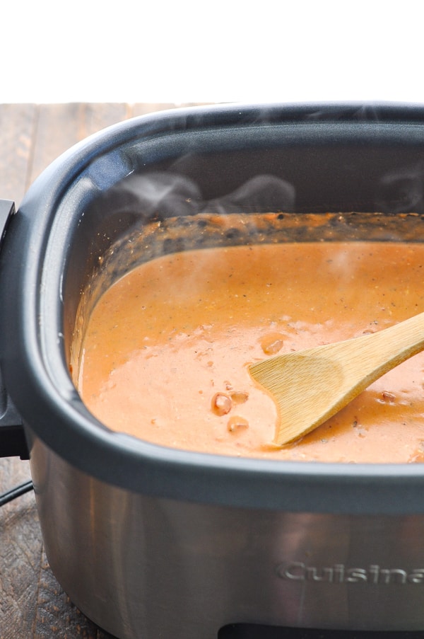 Creamy slow cooker chicken spaghetti sauce in a crock pot with wooden spoon