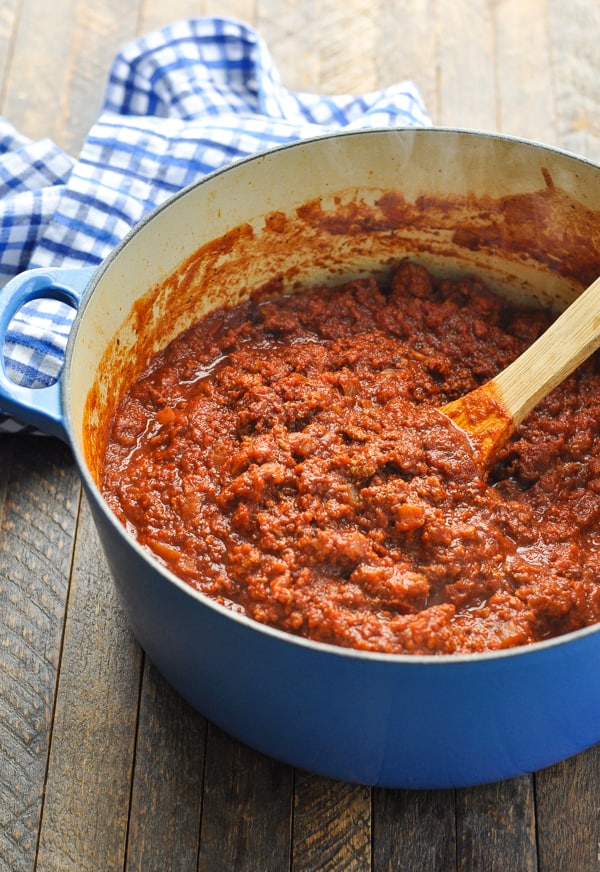 Blue Dutch oven full of spaghetti meat sauce with wooden spoon