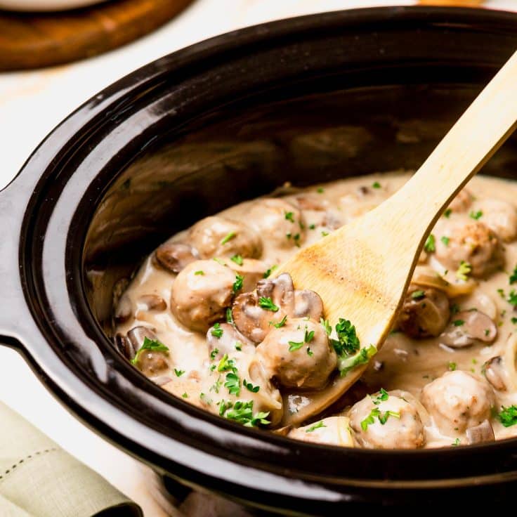 Stirring meatball stroganoff in a Crock Pot.