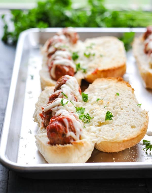 Front view of meatball subs on a sheet pan garnished with parsley
