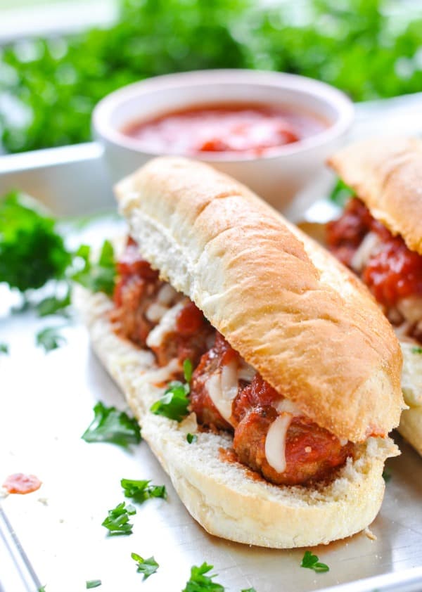 Close up shot of meatball subs on a baking sheet garnished with parsley