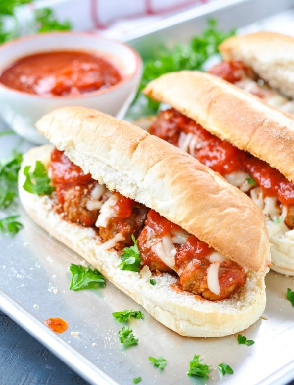 Meatball subs on a baking sheet with marinara sauce in a bowl in the background