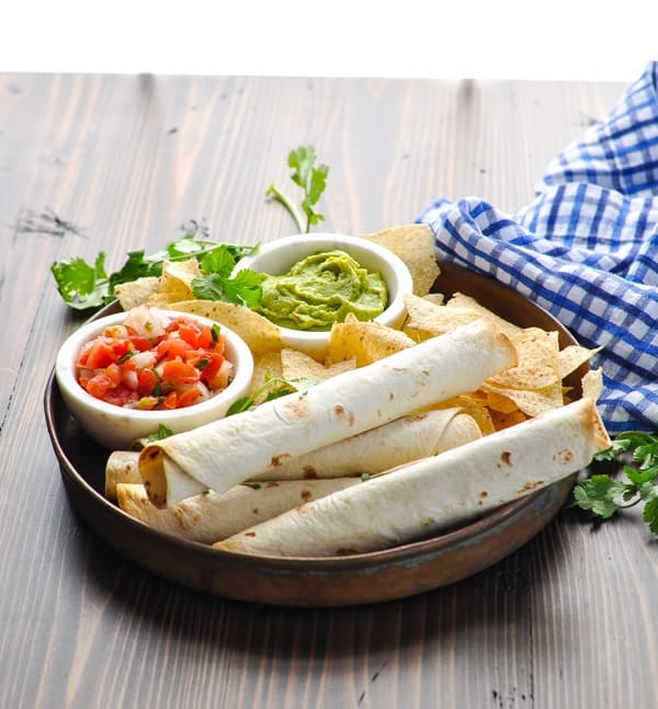 Front view of taquitos on a serving tray with blue and white napkin in background