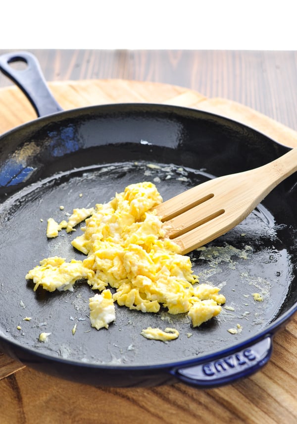 Cooked scrambled eggs in a cast iron skillet with wooden spoon